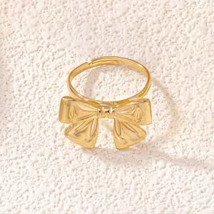Close-up of golden bow-knot ring with adjustable open band on elegant soft fabric