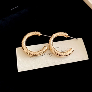 Macro view of gold C-shaped earrings with dotted texture on a black velvet background