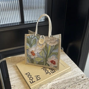 Detail of floral linen tote bag with braided handles on a book over marble surface