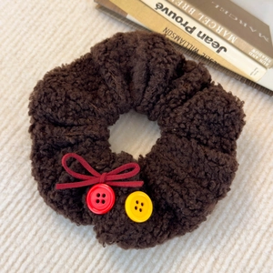 Détail d'un chouchou en peluche marron foncé avec nœud rouge et boutons colorés