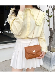 Detail of a brown quilted crossbody bag with a white butterfly clasp and gold chain strap