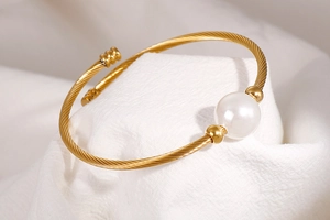 Vue détaillée du bracelet jonc torsadé doré orné d'une perle blanche centrale et de perles
