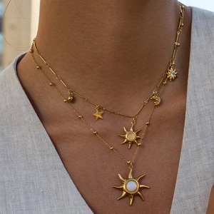 Detail of a layered gold necklace with sun, moon and star pendants featuring opal stones