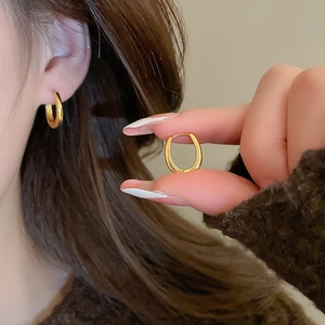 Detailed view of minimalist gold hoop earrings on ear and held between fingers