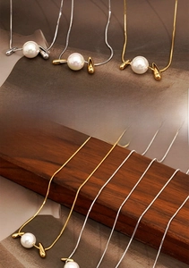 Detail of snake chain necklaces with pearl pendants in gold and silver finishes