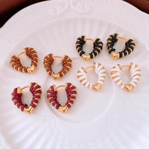 Close-up of heart-shaped earrings in four colors with gold metal woven textures