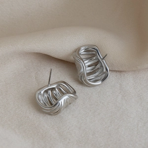 Macro detail of silver C-shaped wave earrings on soft cream silk background