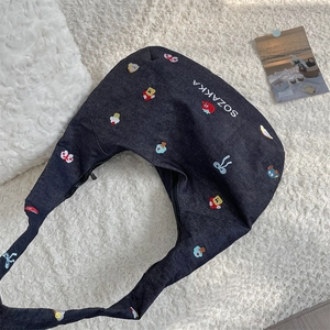 Detail of navy blue denim crescent bag with colorful embroidery on white plush fabric