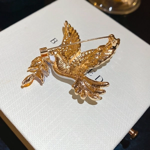 Close-up of golden dove brooch with olive branch and metal pin on white jewelry box