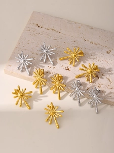 Detailed close-up of gold and silver sunburst stud earrings on a textured stone