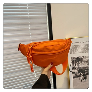 Detail of bright orange nylon crossbody bag with matching zipper and woven rope puller