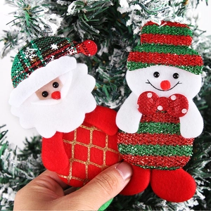 Close-up of handmade plush Santa and snowman ornaments hanging on a snowy Christmas tree