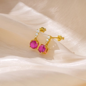 Macro detail of gold earring with round rose red gemstone and sparkling white zirconias