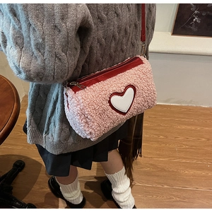 Détail du sac à bandoulière rose en peau de mouton avec écusson cœur blanc et sangle rouge