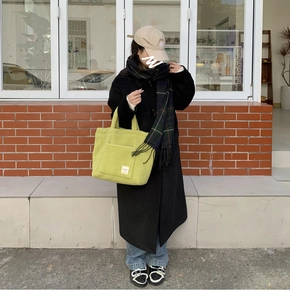 Outdoor shot of a soft yellowish-green lamb wool tote bag styled with a black winter coat