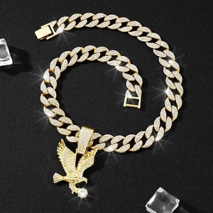 Detail of gold Cuban chain necklace with iced-out eagle pendant on black ice background