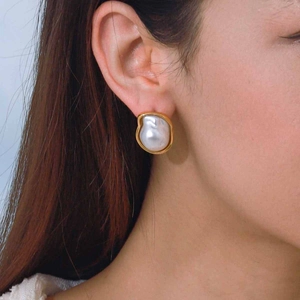 Elegant gold earrings with large white irregular pearls worn by a model in a close-up view
