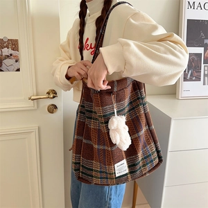 Detail of checkered woolen tote bag featuring a white plush bear charm and side brand label