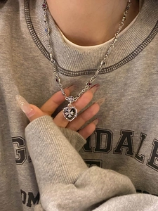 Close-up of silver heart pendant with cross motif on a floral link chain worn by model