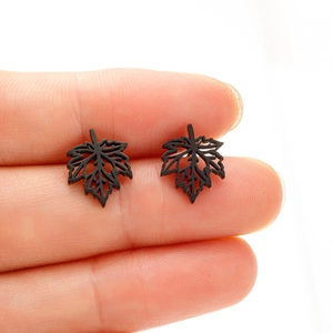 Gros plan de boucles d'oreilles feuilles d'érable noir mat tenues entre les doigts