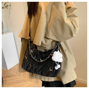 Detail of black pleated tote bag with metal butterfly and white plush cloud pendant