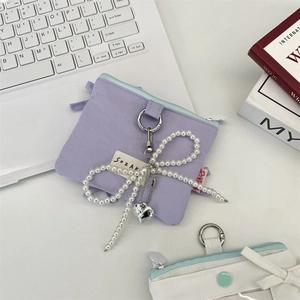 Detail of purple canvas pouch with bow pearl charm and silver heart pendant on a desk