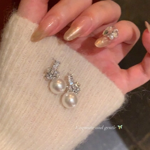 Close-up of elegant white pearl earrings with sparkling rhinestones on knit fabric