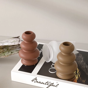 Close-up of modern geometric tiered vases in matte terracotta, olive green and frosted glass
