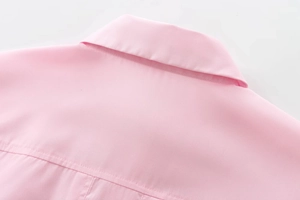 Détail macro du col d'une chemise rose en coton montrant le tissage sergé et la couture