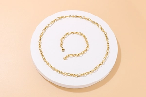 Detail view of gold-tone chain necklace and bracelet set on a white circular podium