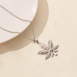Close-up of silver stainless steel leaf pendant necklace on a minimalist ceramic plate