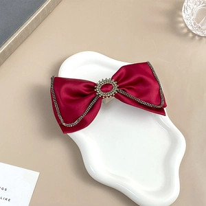 Detail of red velvet bow hair clip featuring rhinestone trim on a white ceramic tray