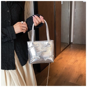 Detail of silver square handbag with metallic finish and cute bow decorations