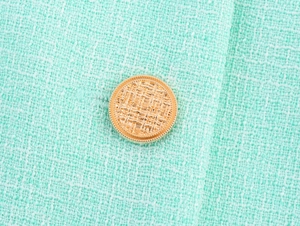 Gros plan sur la texture du tissu tweed vert menthe avec un bouton doré décoratif