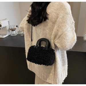 Macro detail of the fuzzy black plush texture and rigid handle on a box-style handbag