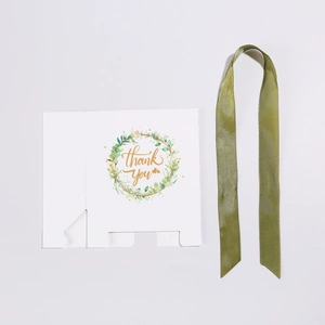 Flat lay of white gift box with eucalyptus thank you wreath and green ribbon
