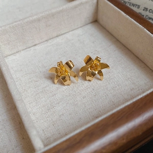 Close-up of golden lily flower stud earrings with brushed metal petals and pollen detail