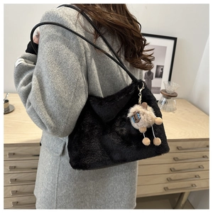 Close-up of black plush tote bag with a cute beige alpaca charm on a grey suit model