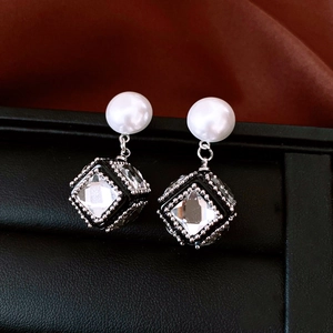 Macro view of geometric square pearl earrings with sparkling cubic pendants in vintage style