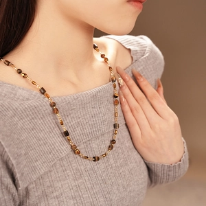 Detail showing the brown tiger eye beaded necklace on model neck in warm studio lighting