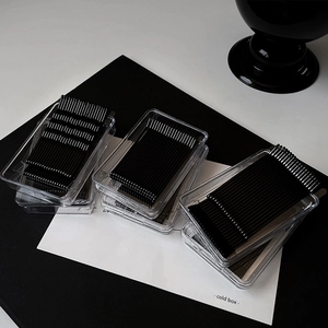 Close-up of black metal hair clips in transparent plastic storage boxes on white surface