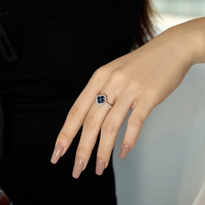 Detailed close-up of a silver four-leaf clover ring with blue stone on a finger