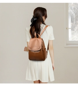 Rear view of a model wearing the brown leather backpack against a clean white wall