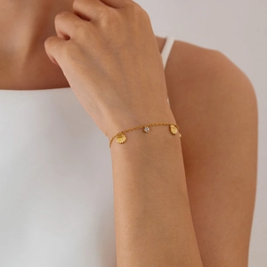 Detailansicht eines goldenen Gliederkettenarmbands mit Muschelanhängern und Zirkon-Stein