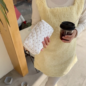 Detail of quilted floral makeup bag in white fabric held by a hand in soft natural light