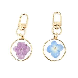Detailed close-up of gold keychains with purple and blue dried flowers in resin charms