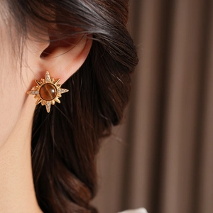 Close-up of golden sunburst earring with tiger eye stone and crystals on a model