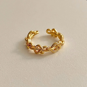 Detail of a minimalist gold braided knot open ring with a high-polished metallic finish