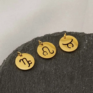 Detailed view of three gold-plated hollow zodiac pendants on a grey stone surface