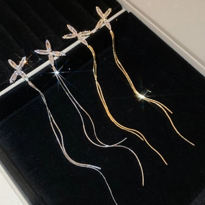 Détail de boucles d'oreilles à pompons en X en or et argent dans un écrin de velours noir